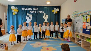Dzieci stoją na scenie ubrani w biało żółte stroje